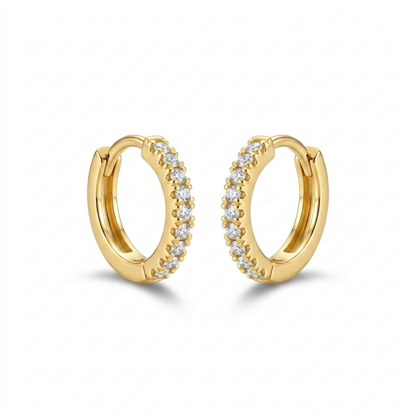 A pair of gold-plated huggie hoop earrings for women featuring a delicate row of clear crystals, shown on a white background