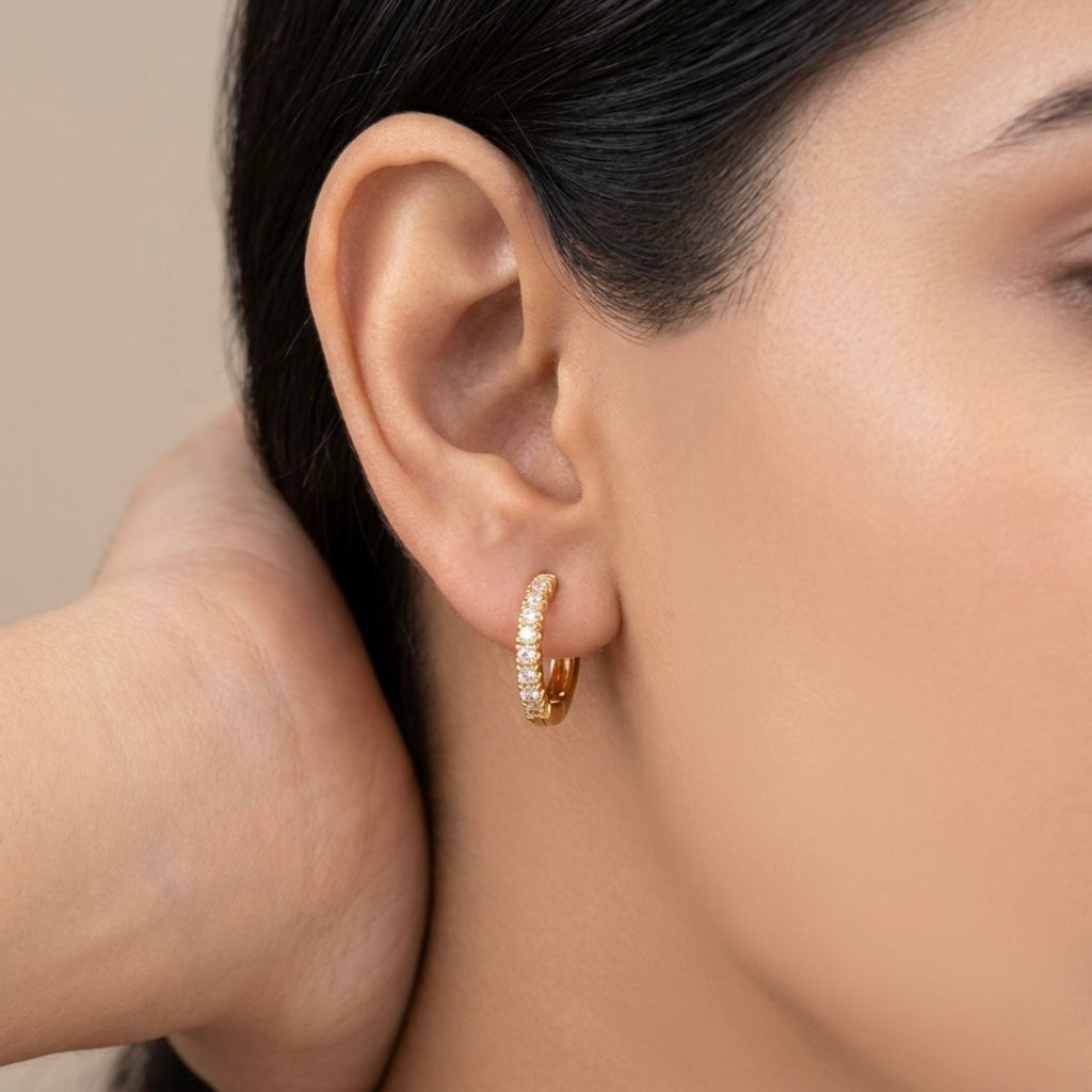 A gold-plated huggie hoop earrings for women featuring a delicate row of clear crystals, shown on a model