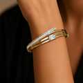 A layered gold-plated bracelet for women featuring a triple-band design with pavé crystals and a central baguette stone, shown on a model