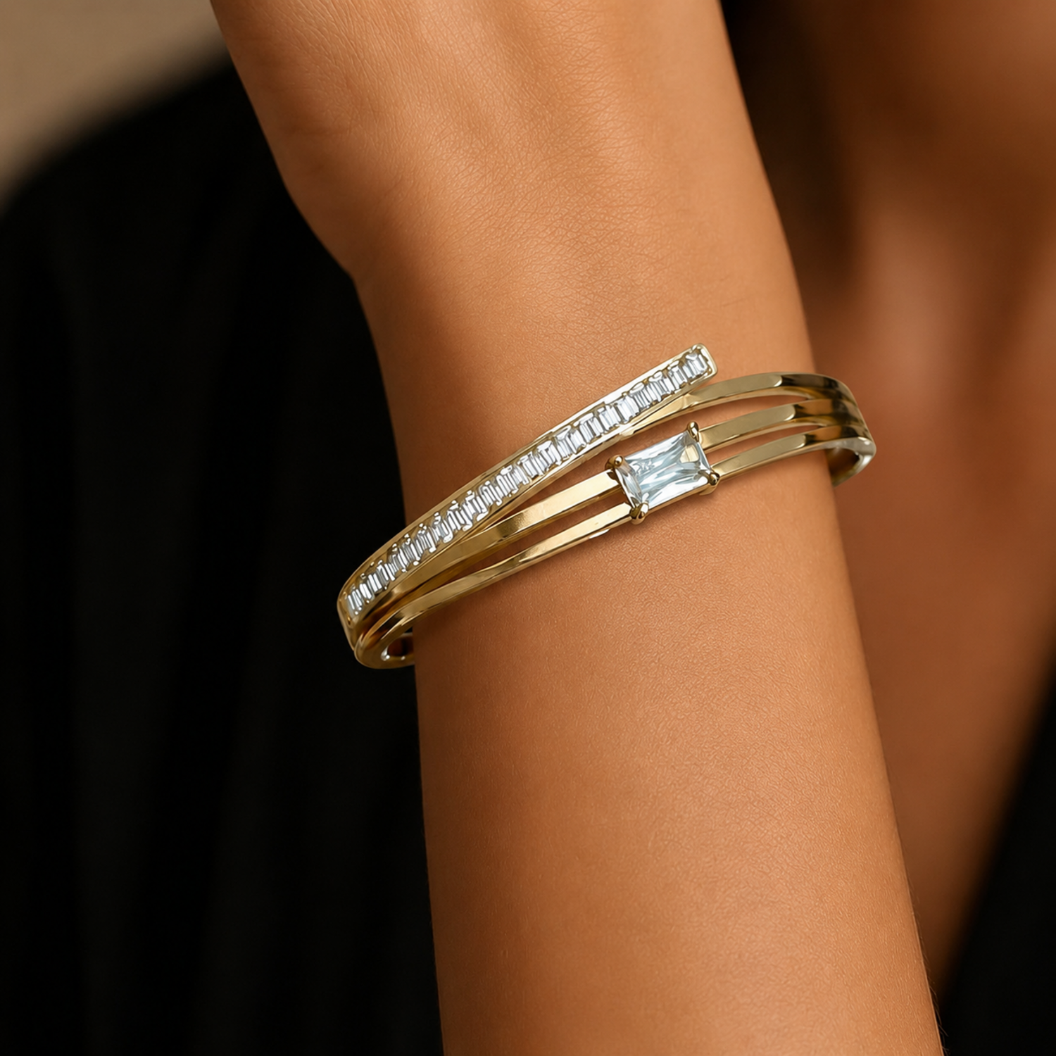 A layered gold-plated bracelet for women featuring a triple-band design with pavé crystals and a central baguette stone, shown on a model