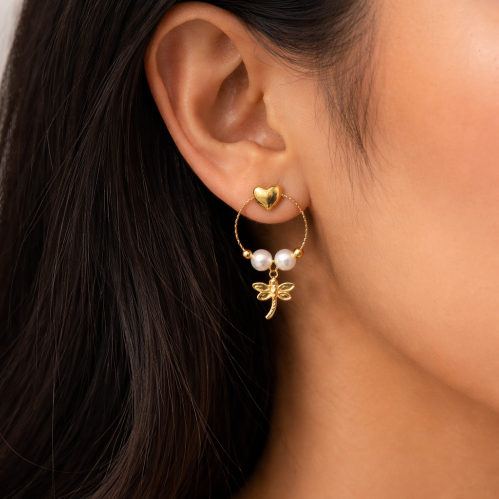 A gold-plated earrings for women featuring a detailed dragonfly charm and three white pearls, shown on a model
