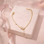 A dainty gold-plated chain bracelet for women featuring a white butterfly charm and crystal accents on a soft pink background.
