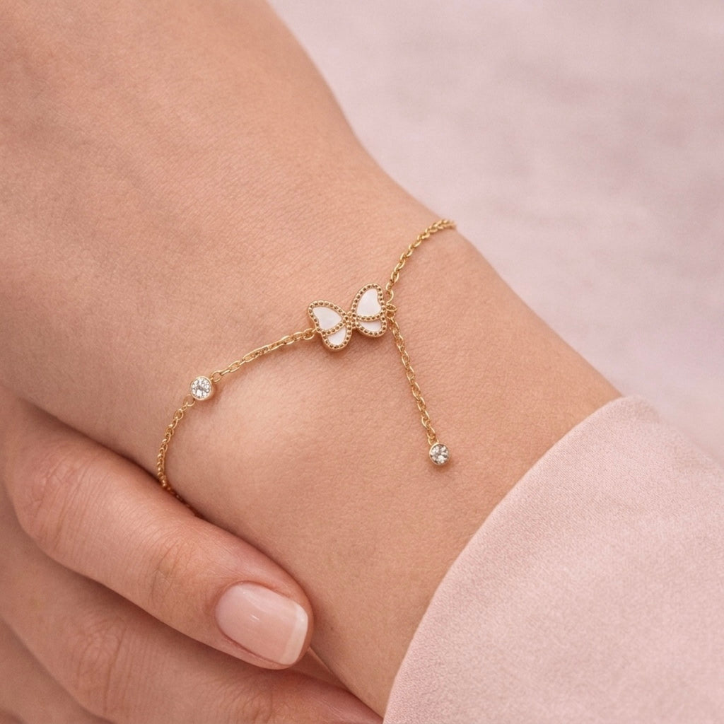 A dainty gold-plated chain bracelet for women featuring a white butterfly charm and crystal accents on a model