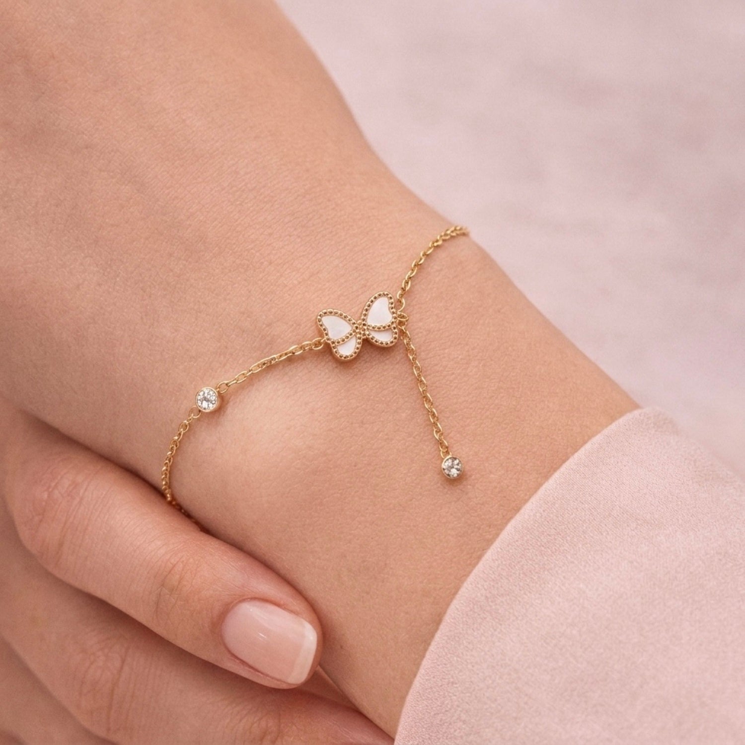 A dainty gold-plated chain bracelet for women featuring a white butterfly charm and crystal accents on a model