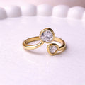 Gold plated adjustable ring for women featuring two heart-cut white stones of different sizes in a bypass wrap design, displayed on a white surface