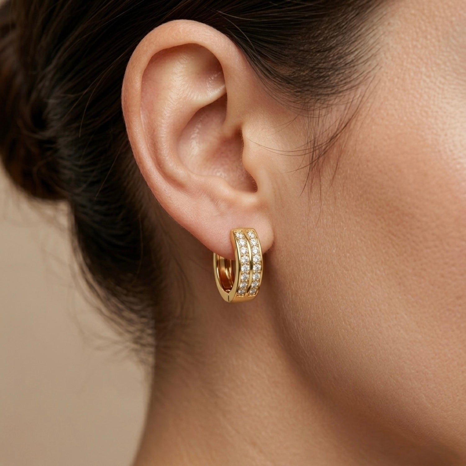 A gold-plated huggie hoop earrings for women featuring a duo design set with clear crystals, shown on a model