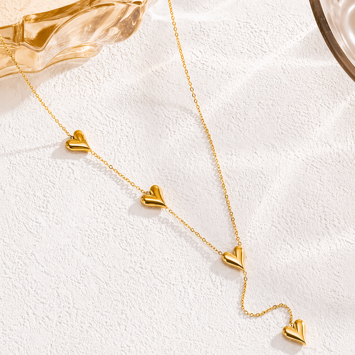 Gold necklace with heart-shaped pendants on a white textured surface