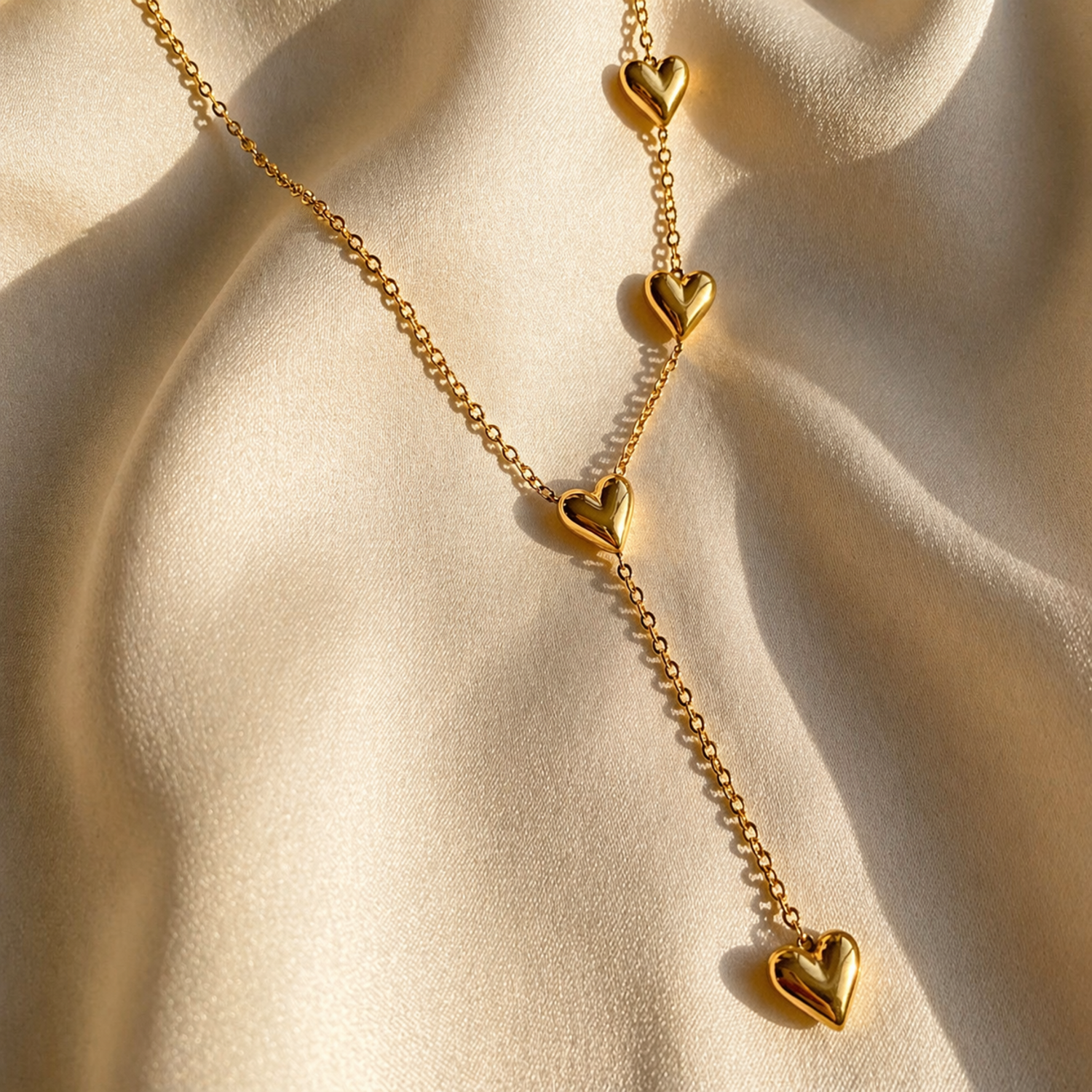 Gold necklace with heart-shaped pendants on a beige fabric background