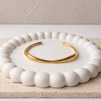 A minimalist gold-plated adjustable cuff bracelet for women featuring a slim, organic wave design on a white ceramic dish