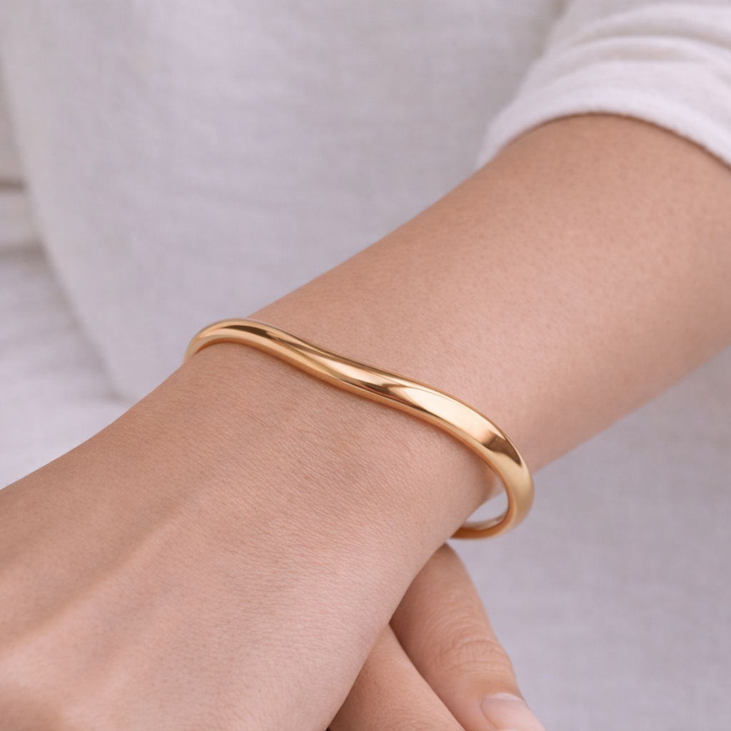 A minimalist gold-plated adjustable cuff bracelet for women featuring a slim, organic wave design on a model hand
