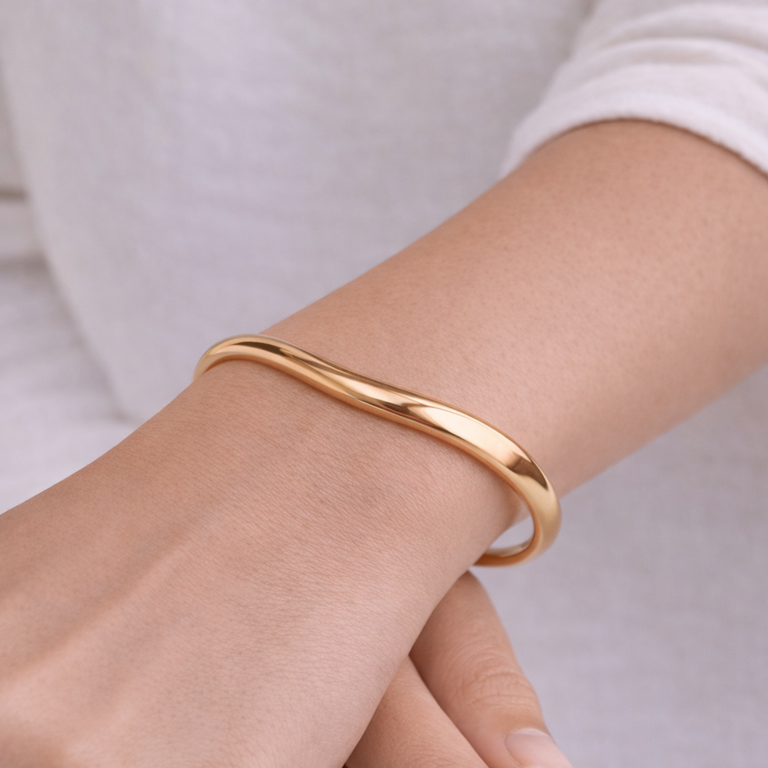 A minimalist gold-plated adjustable cuff bracelet for women featuring a slim, organic wave design on a model hand