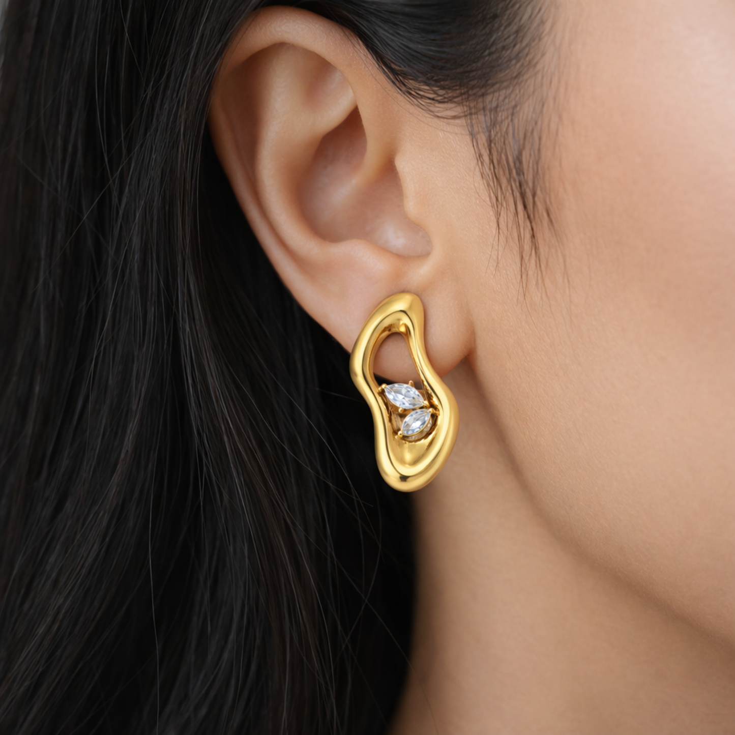 A gold-plated abstract-shaped stud earrings for women featuring two marquise crystals inside a molten gold frame, shown on a model