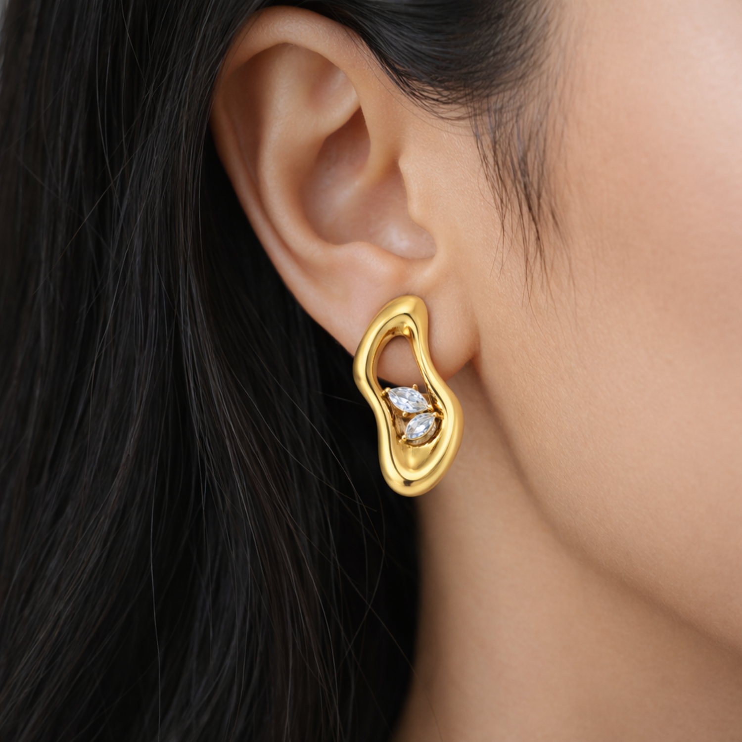 A gold-plated abstract-shaped stud earrings for women featuring two marquise crystals inside a molten gold frame, shown on a model