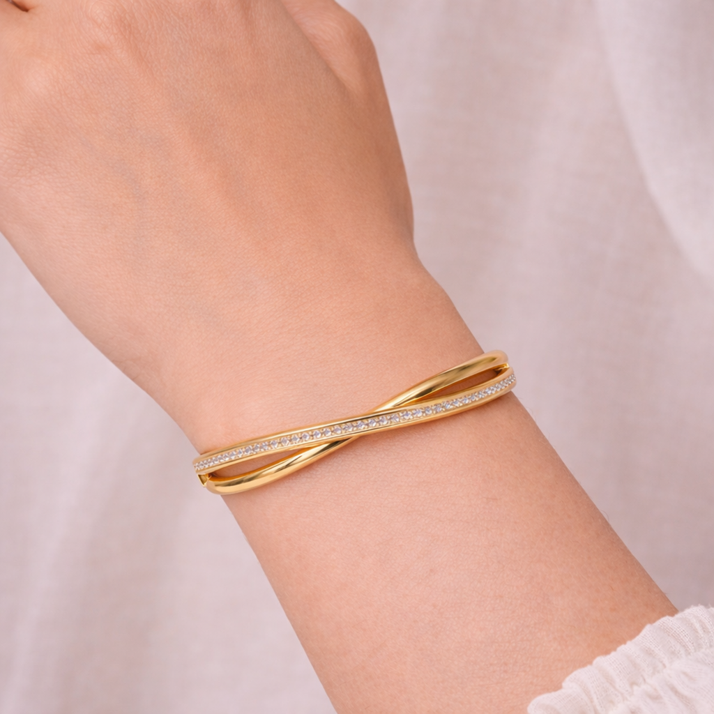 A luxurious gold-plated double-band cross-over bangle for women featuring one polished strand and one strand of brilliant pavé white stones displayed on a model hand