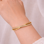 A luxurious gold-plated double-band cross-over bangle for women featuring one polished strand and one strand of brilliant pavé white stones displayed on a model hand