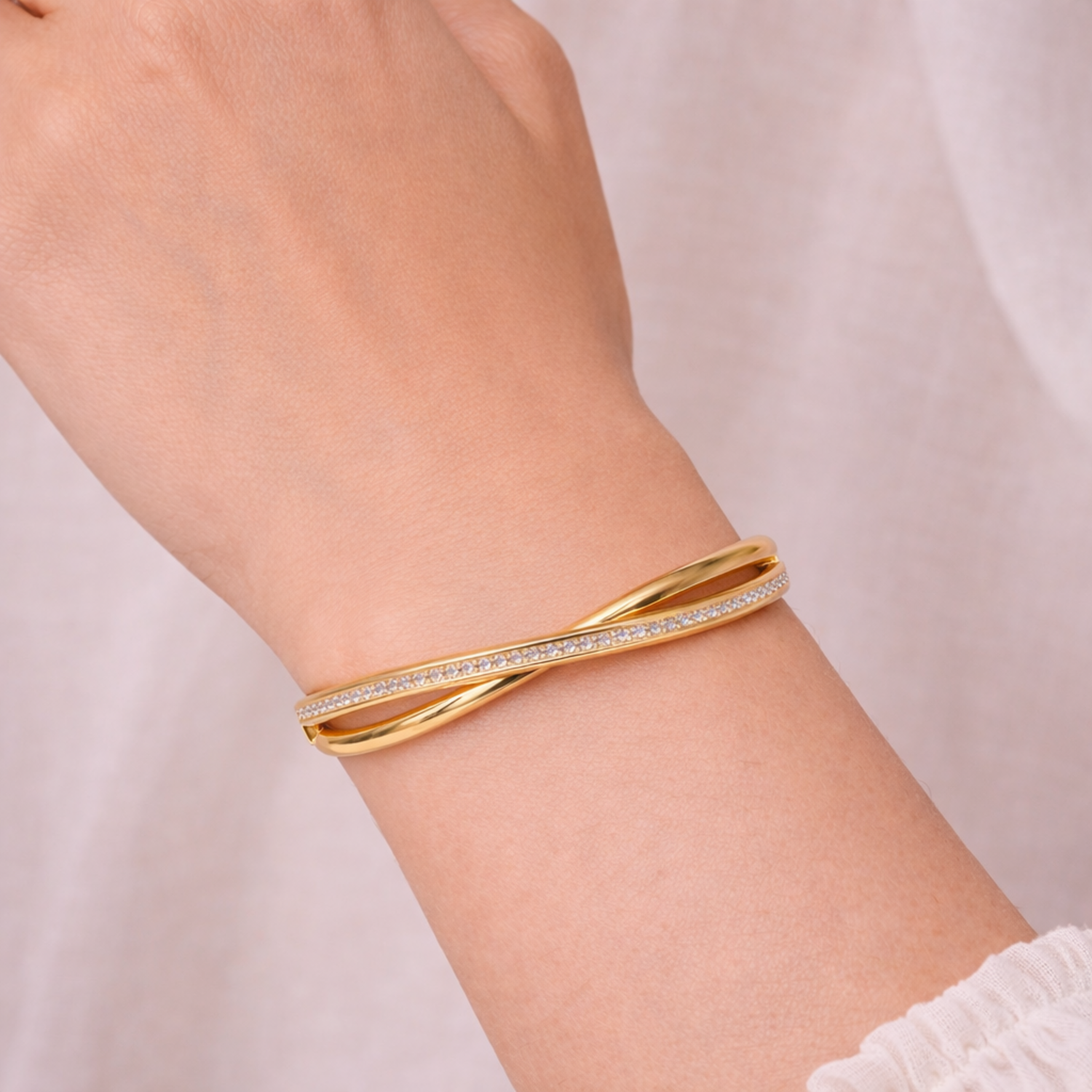 A luxurious gold-plated double-band cross-over bangle for women featuring one polished strand and one strand of brilliant pavé white stones displayed on a model hand