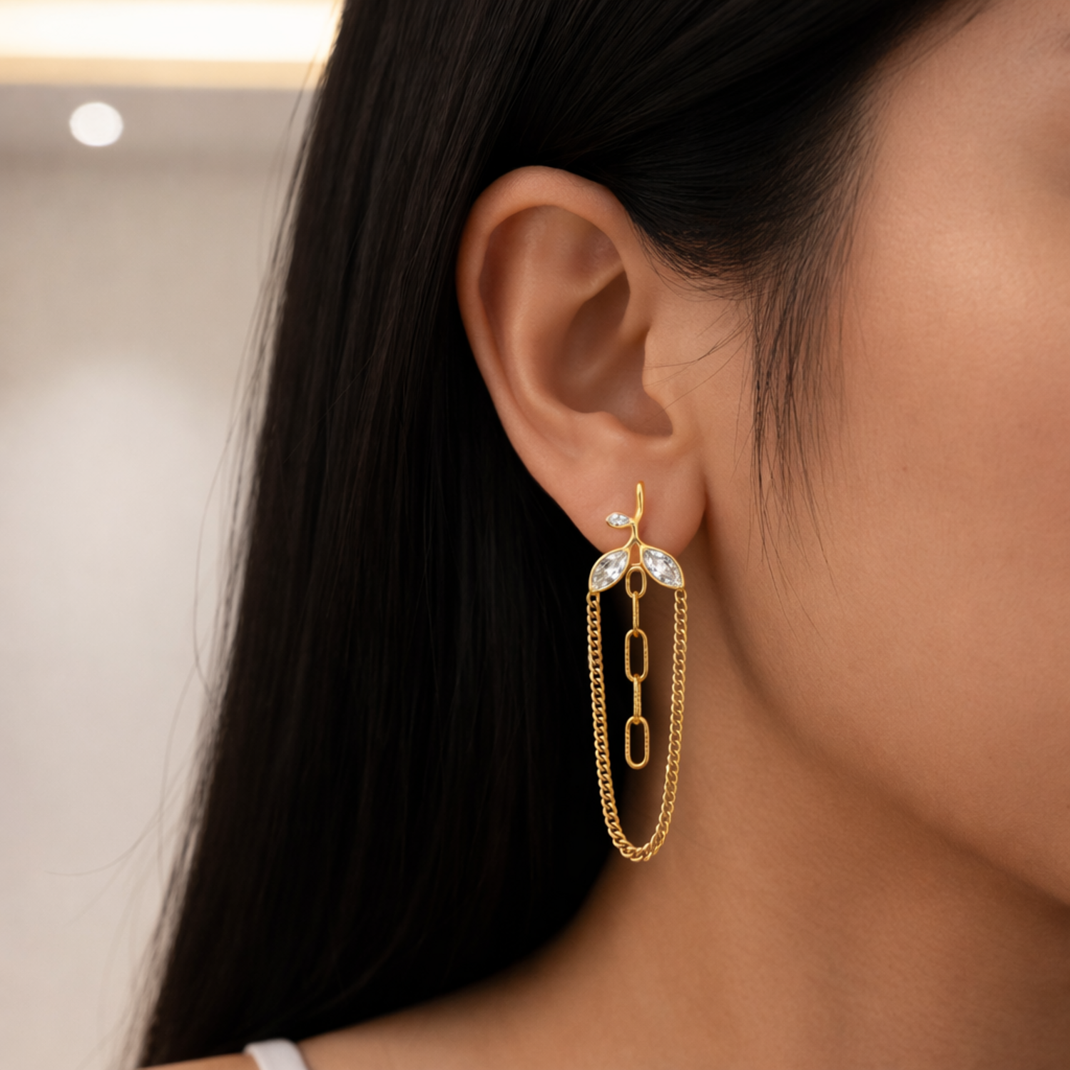 A gold-plated long earrings for women featuring a three-leaf crystal vine that suspends a cascading gold curb chain loop and central paperclip links on a model