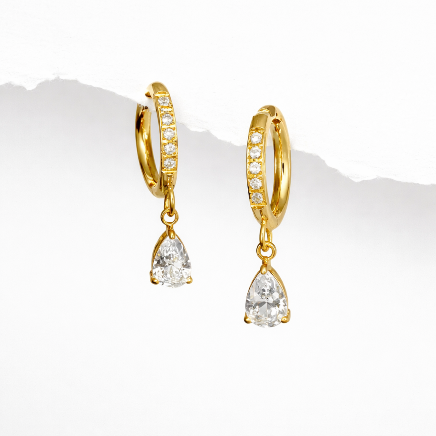 A pair of gold-plated hoop earrings for women featuring a sparkling pear-cut crystal drop, shown on a white background