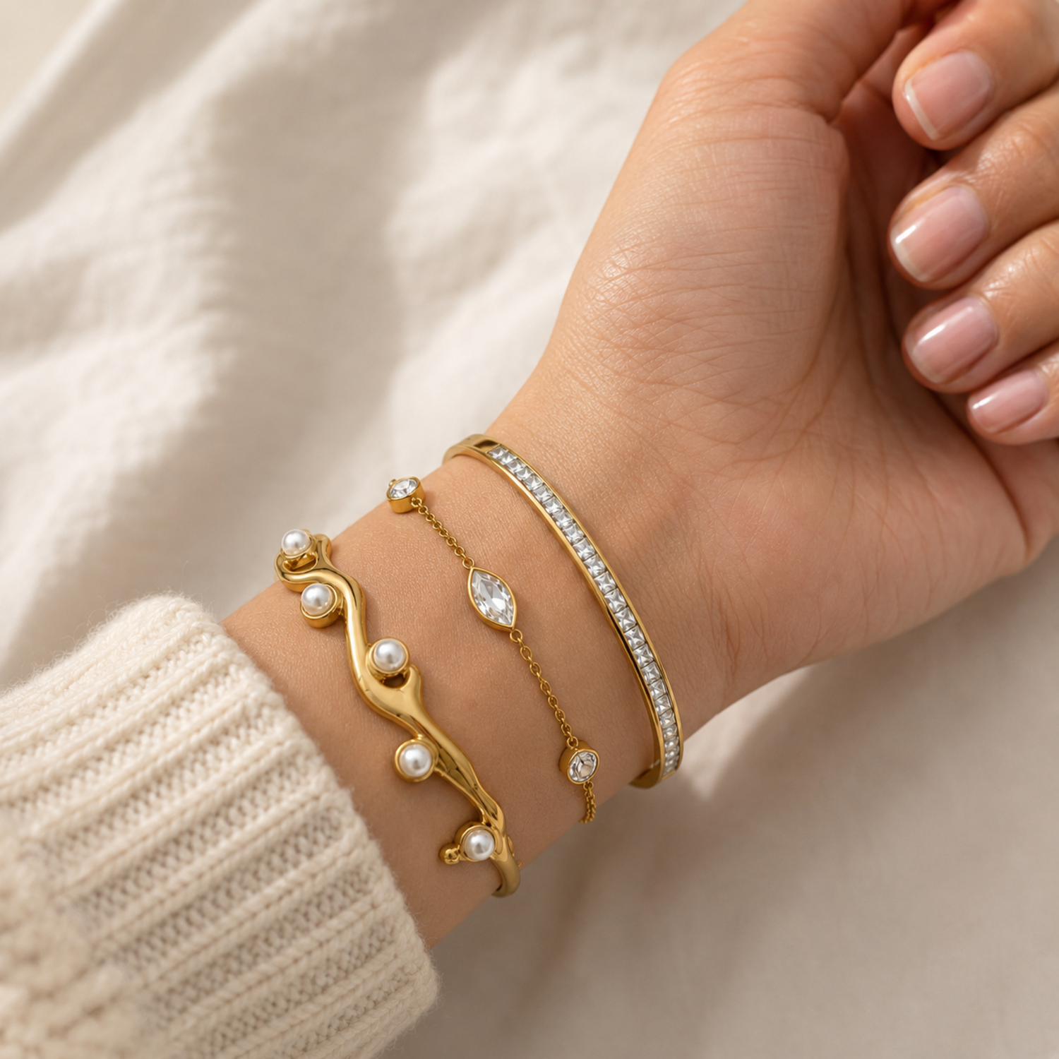 A three-piece gold-plated wrist stack for women featuring a minimalist open cuff, a solid polished kada, and a delicate bezel-set crystal chain bracelet, on a model hand