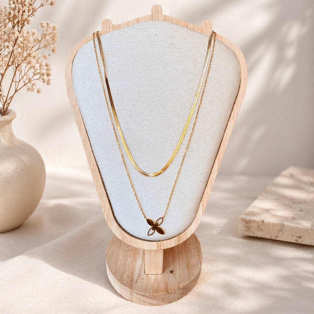 Gold plated layered necklace with flower pendant on a wooden stand with a light background