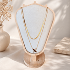 Gold plated layered necklace with flower pendant on a wooden stand with a light background