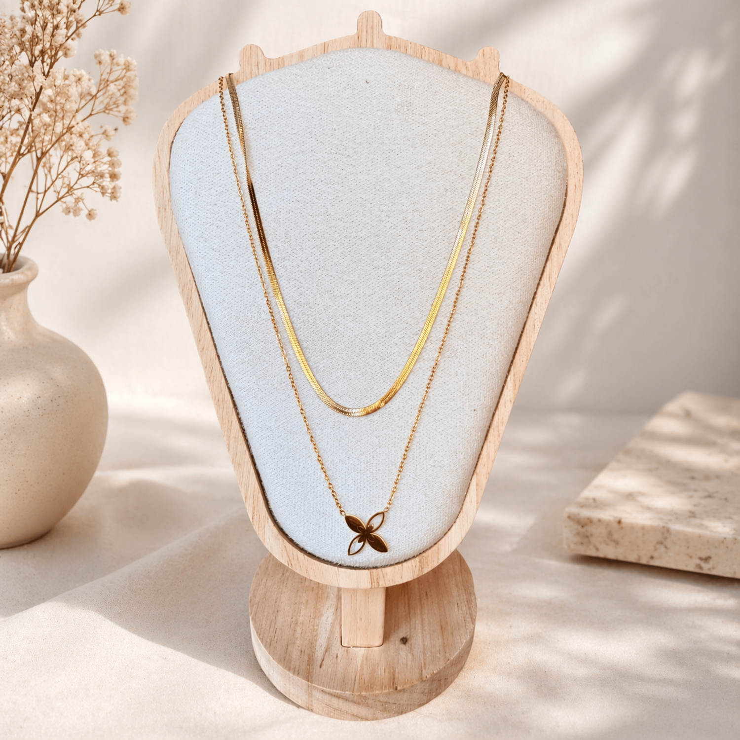 Gold plated layered necklace with flower pendant on a wooden stand with a light background