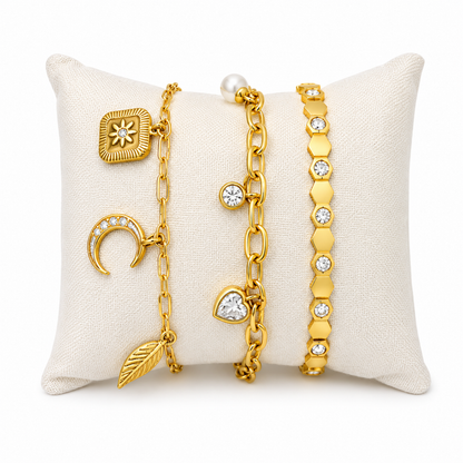 A three-piece gold-plated bracelet stack for women featuring a celestial charm link chain, a chunky paperclip charm chain with a pearl and heart drop, and a geometric honeycomb crystal bangle.