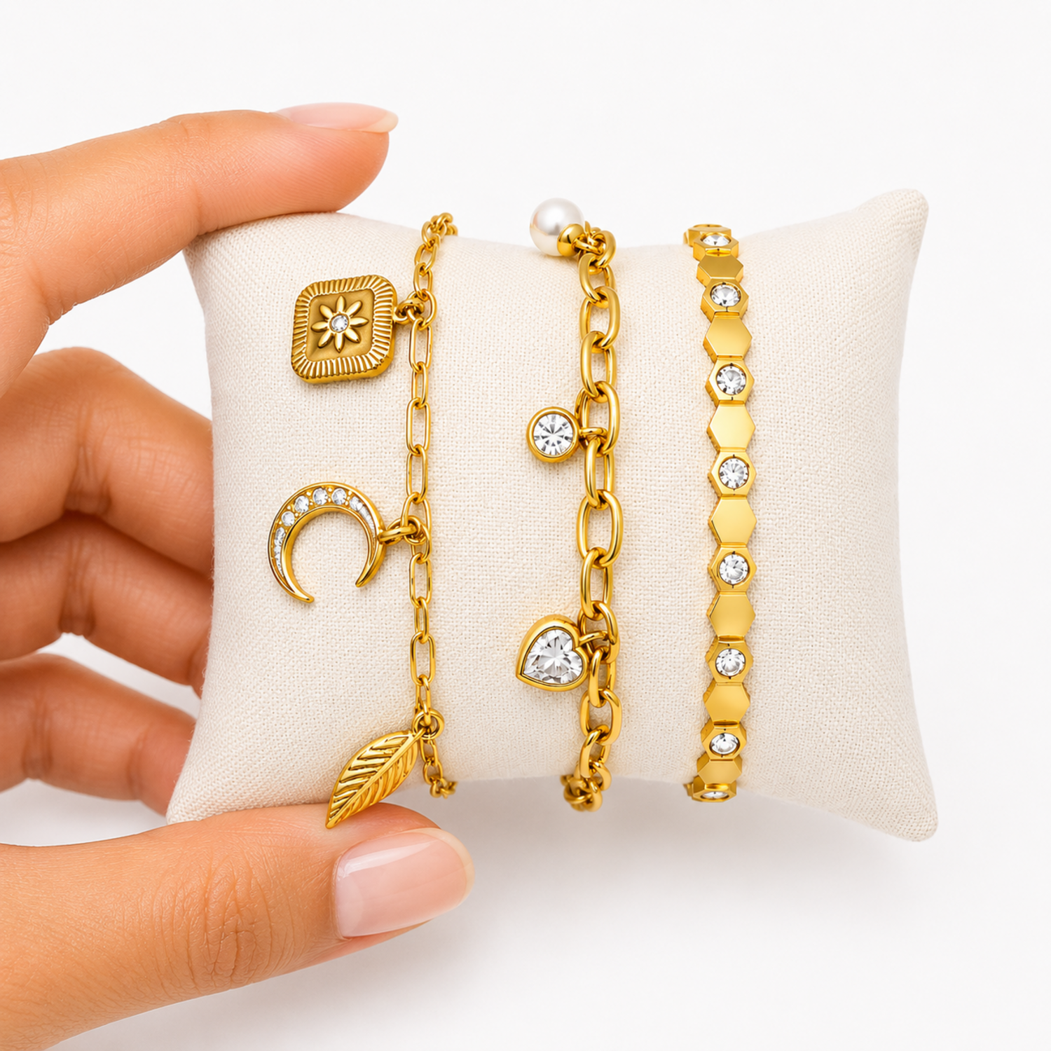 A close-view of a three-piece gold-plated bracelet stack for women featuring a celestial charm link chain, a chunky paperclip charm chain with a pearl and heart drop, and a geometric honeycomb crystal bangle.