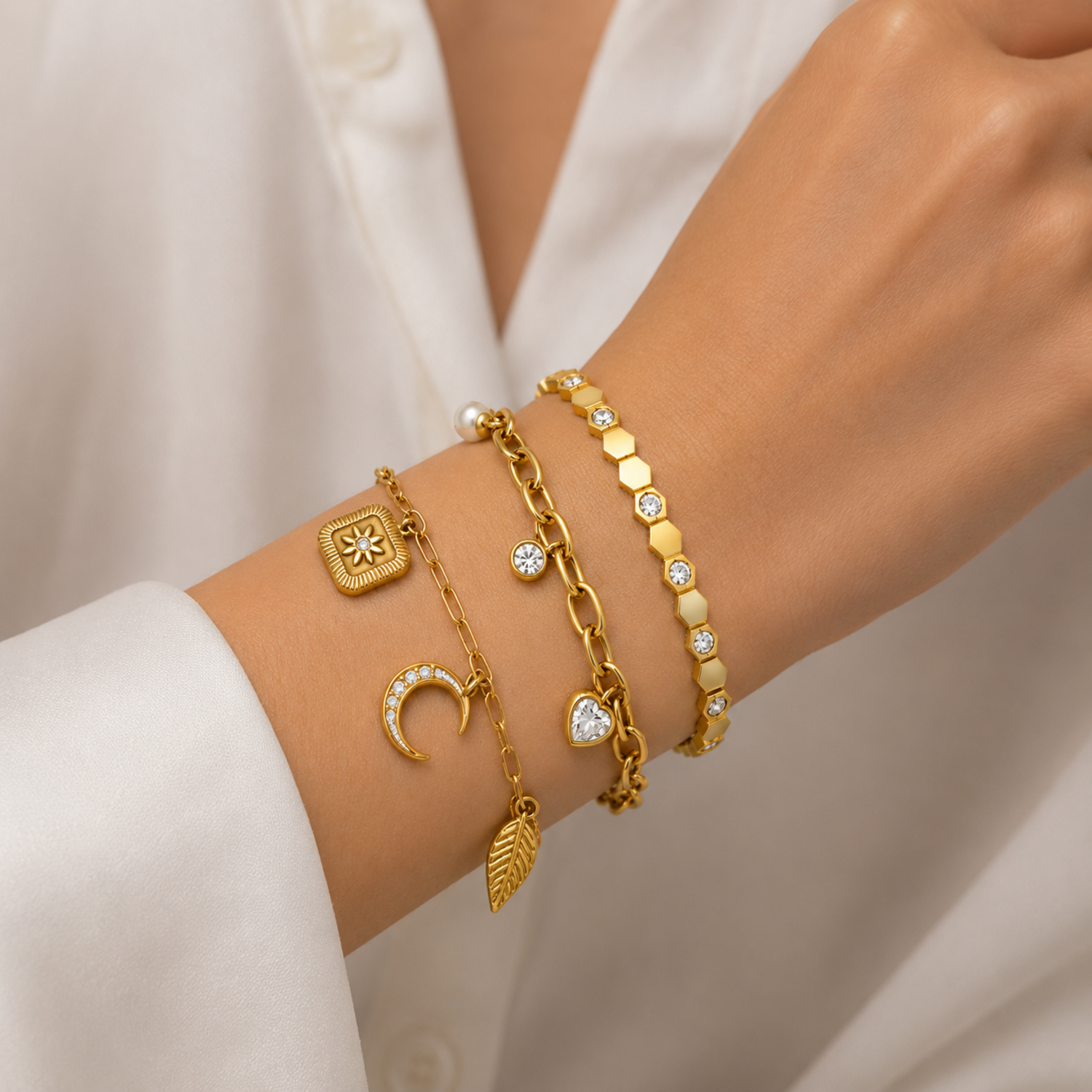 A three-piece gold-plated bracelet stack for women featuring a celestial charm link chain, a chunky paperclip charm chain with a pearl and heart drop, and a geometric honeycomb crystal bangle, on a model