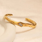 A gold-plated organic texture open-cuff bracelet for women featuring a central crystal solitaire.