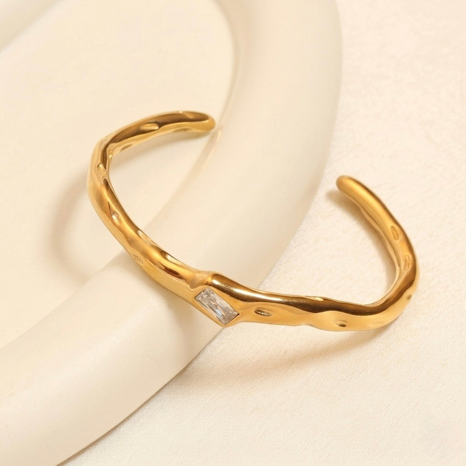 A gold-plated organic texture open-cuff bracelet for women featuring a central crystal solitaire.