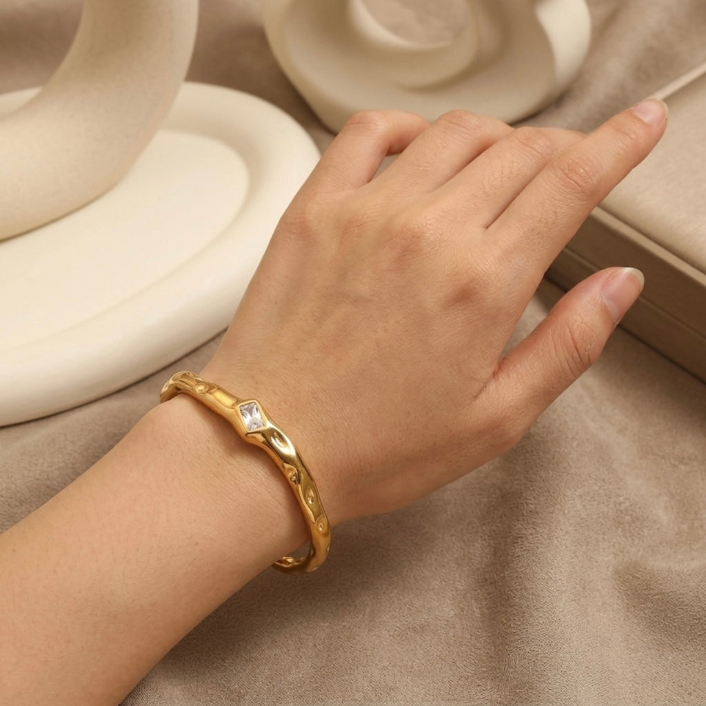 A gold-plated organic texture open-cuff bracelet for women featuring a central crystal solitaire, shown on a model