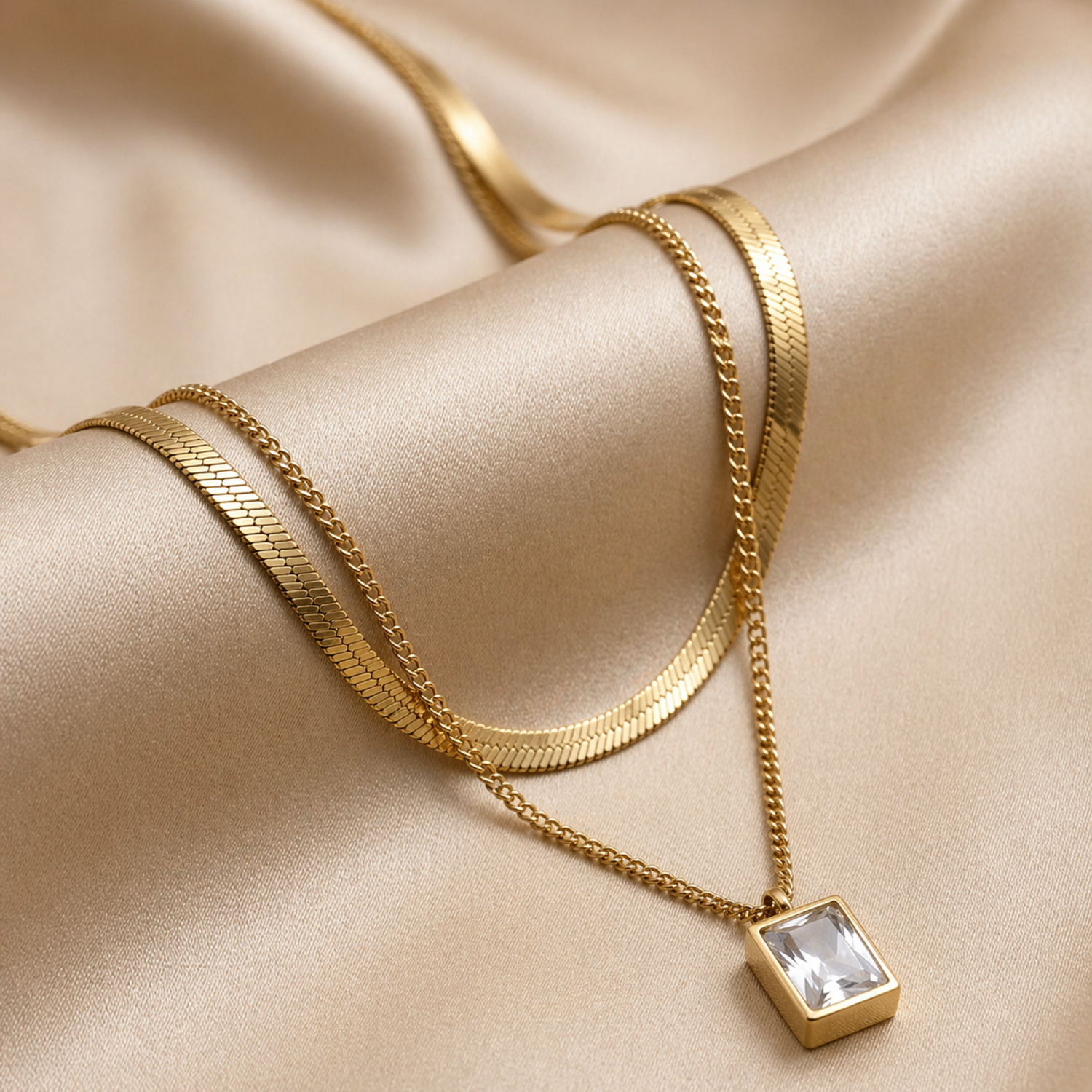 A gold-plated stainless steel chain for women featuring a layered necklace design with a flat herringbone chain and a link chain holding an emerald-cut crystal pendant