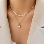 A gold-plated stainless steel chain for women featuring a layered necklace design with a flat herringbone chain and a link chain holding an emerald-cut crystal pendant