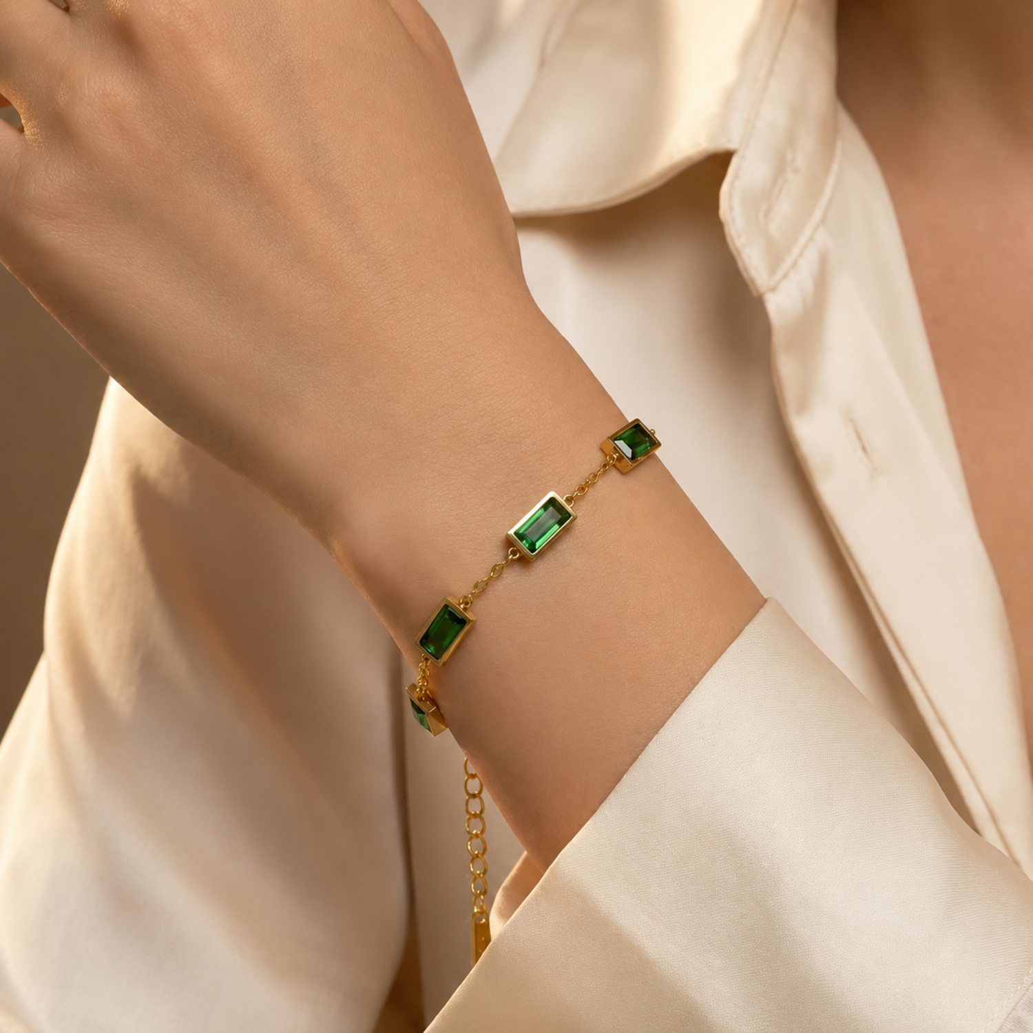 A close-view of a gold-plated stainless steel chain bracelet for women featuring five rectangular emerald-green baguette stones