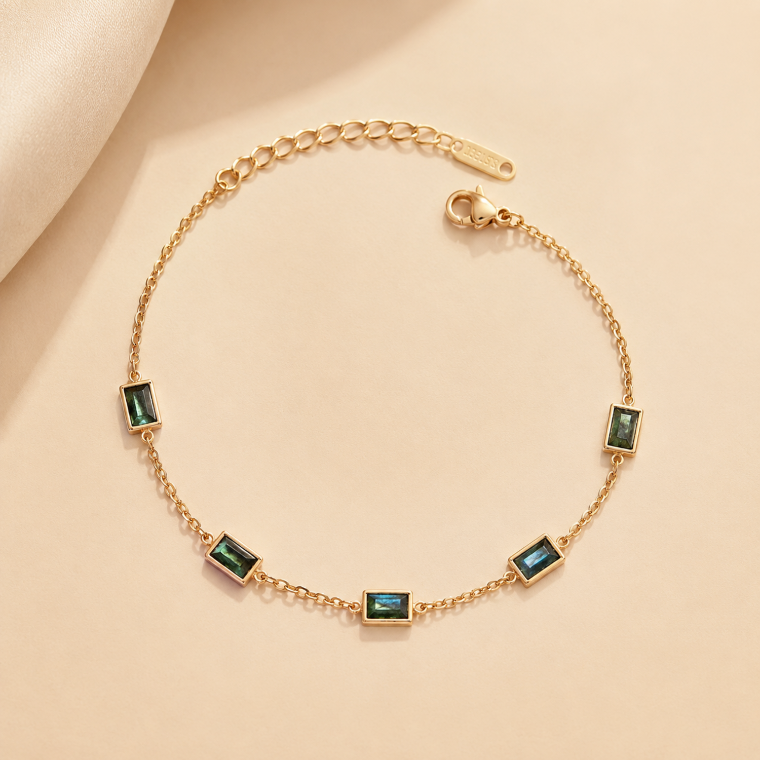 A gold-plated stainless steel chain bracelet for women featuring five rectangular emerald-green baguette stones.