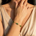 A gold-plated stainless steel chain bracelet for women featuring five rectangular emerald-green baguette stones, shown on a model