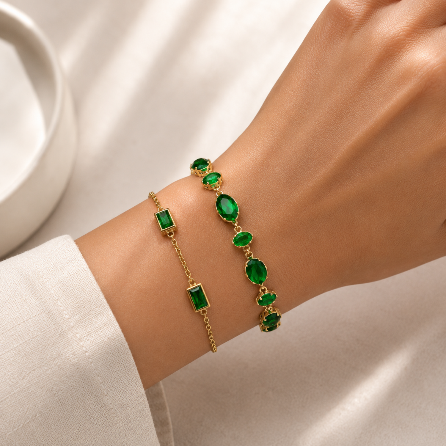A premium two-piece gold-plated bracelet stack for women featuring the Emerald Horizon Baguette Bracelet and a matching faceted emerald green oval crystal chain bracelet, on a model