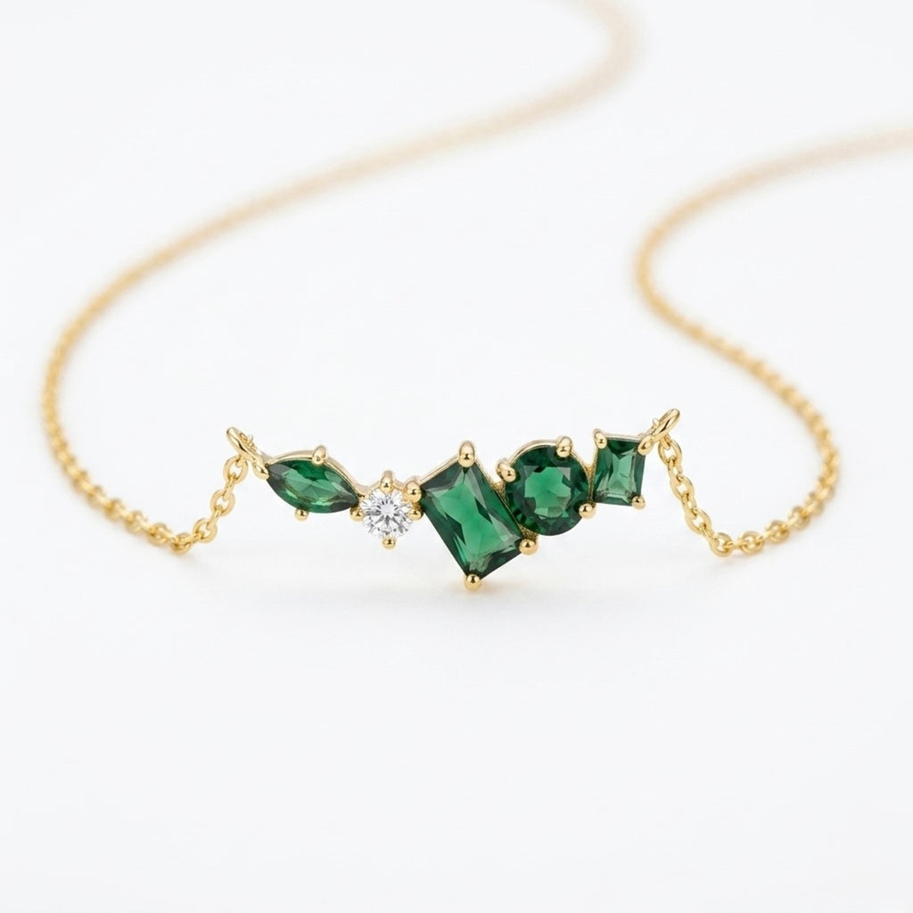 A close-view of a gold-plated stainless steel chain for women featuring an asymmetrical pendant bar set with various emerald green and white crystal stones.
