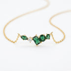 A close-view of a gold-plated stainless steel chain for women featuring an asymmetrical pendant bar set with various emerald green and white crystal stones.