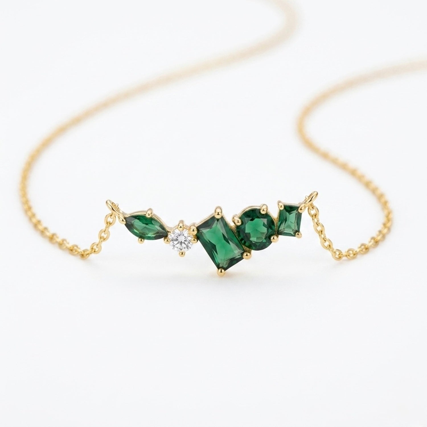 A close-view of a gold-plated stainless steel chain for women featuring an asymmetrical pendant bar set with various emerald green and white crystal stones.