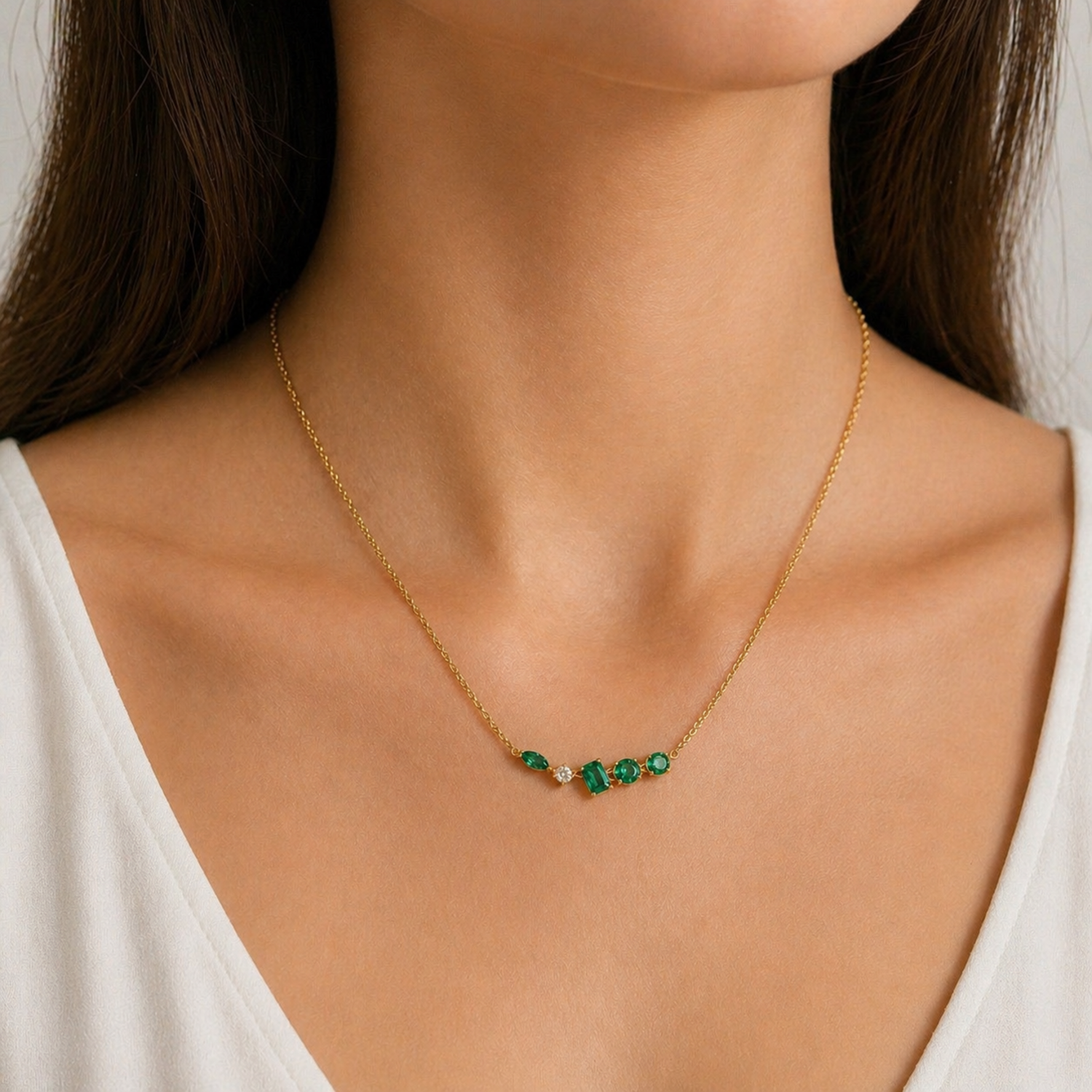 A gold-plated stainless steel chain for women featuring an asymmetrical pendant bar set with various emerald green and white crystal stones, shown on a model