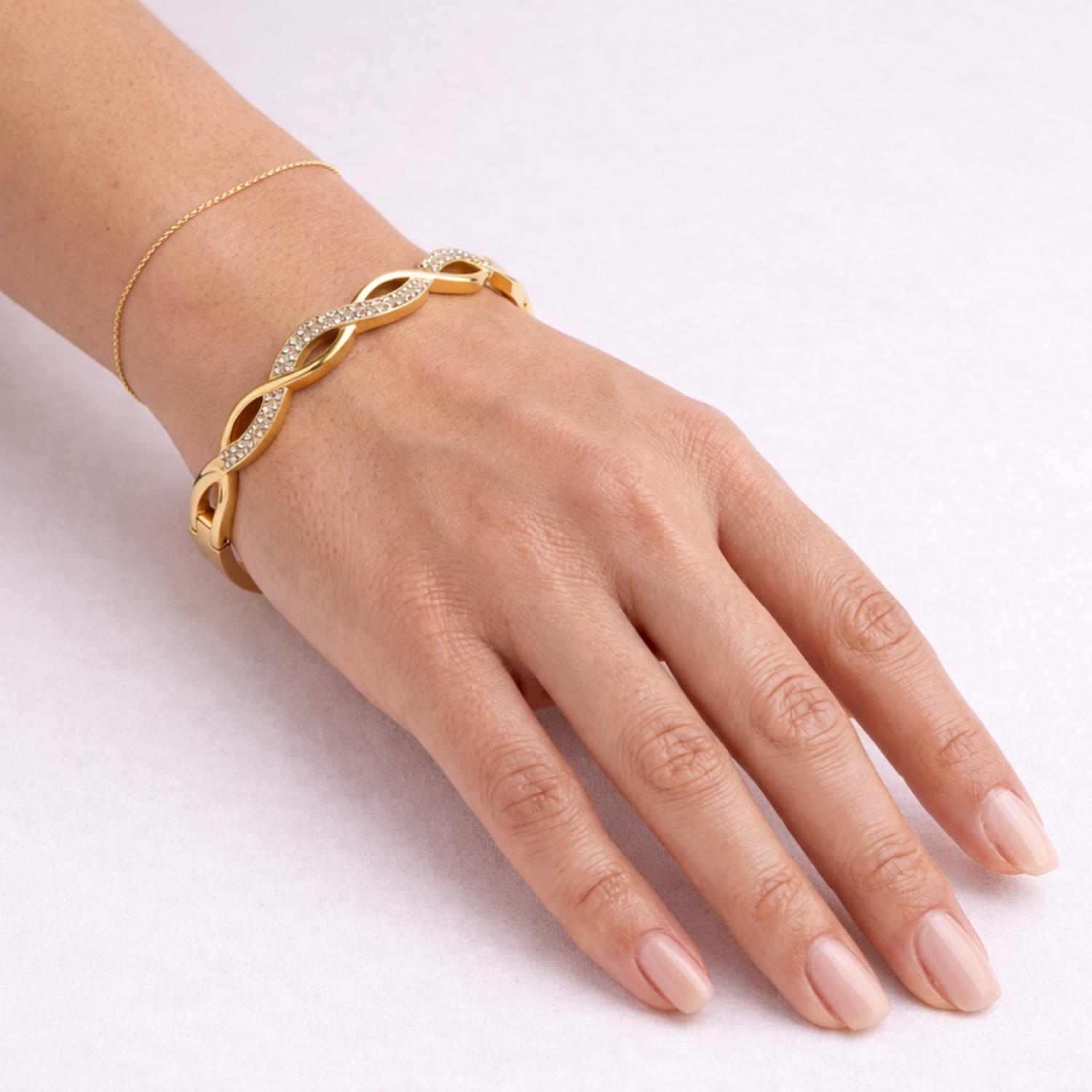 A close-view of a high-quality gold-plated infinity braid bangle for women featuring pavé-set white stones on a white background