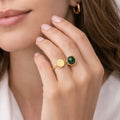 Close-up of a unique asymmetrical open band and a forest green circular stone gold-plated ring for women showcased on a model