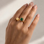 Close-up of a contemporary gold-plated ring for women, showcasing a unique asymmetrical open band and a forest green circular stone