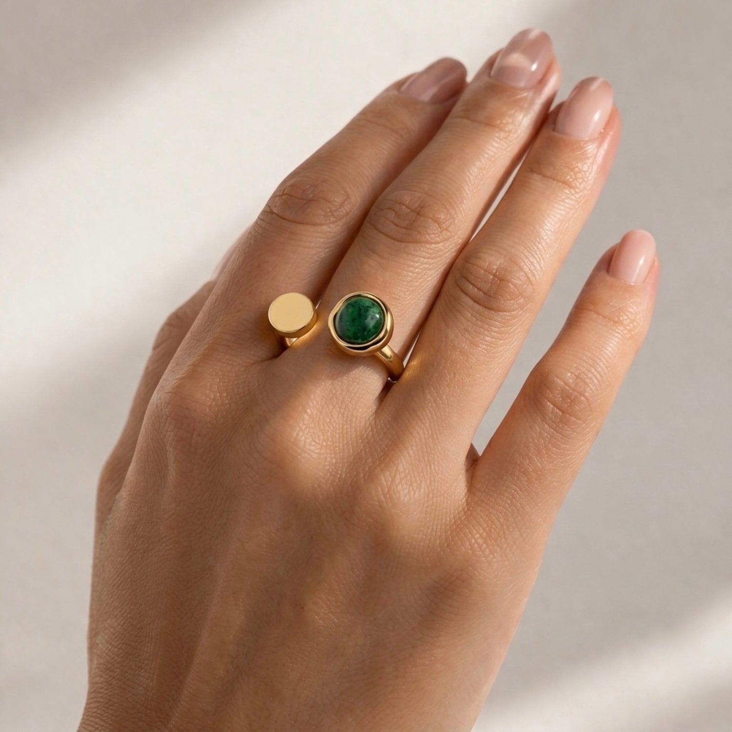 Close-up of a contemporary gold-plated ring for women, showcasing a unique asymmetrical open band and a forest green circular stone