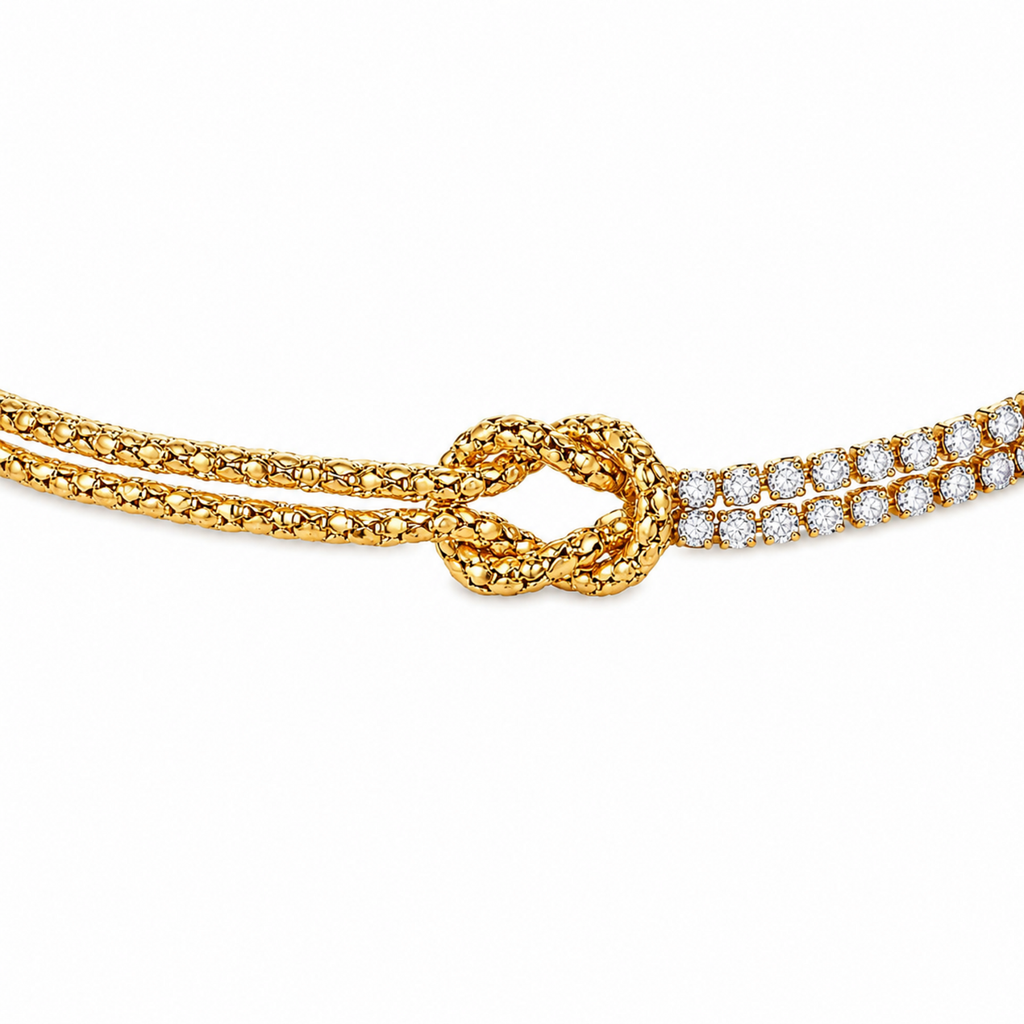 A close-view of a gold-plated chain bracelet for women featuring a central knot, one woven gold strand, and one double-row crystal strand.