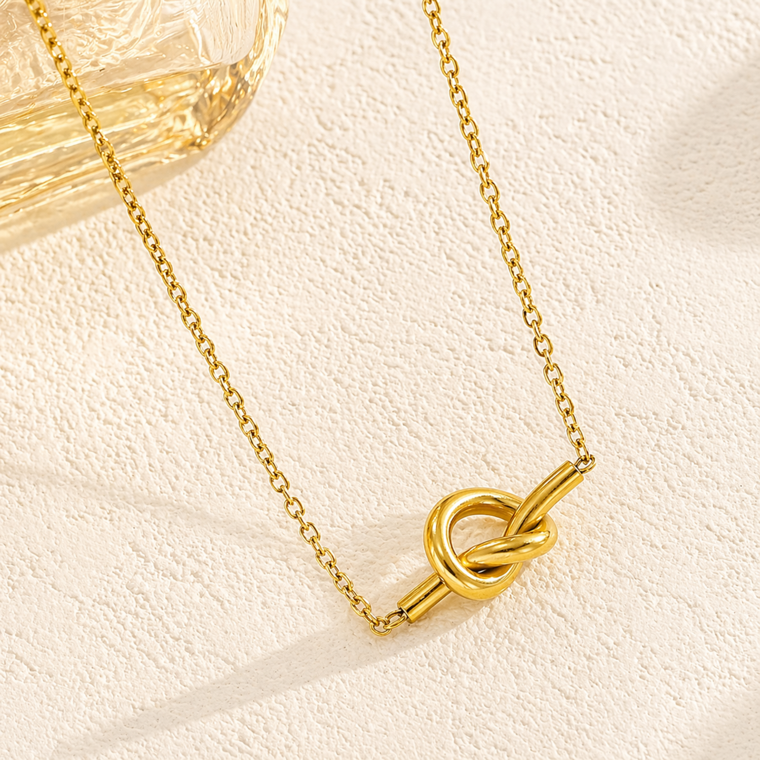 A close-view of a gold-plated stainless steel chain for women featuring a polished, sculptural knot pendant on a delicate link chain