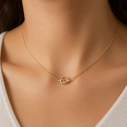 A gold-plated stainless steel chain for women featuring a polished, sculptural knot pendant on a delicate link chain, on a model.
