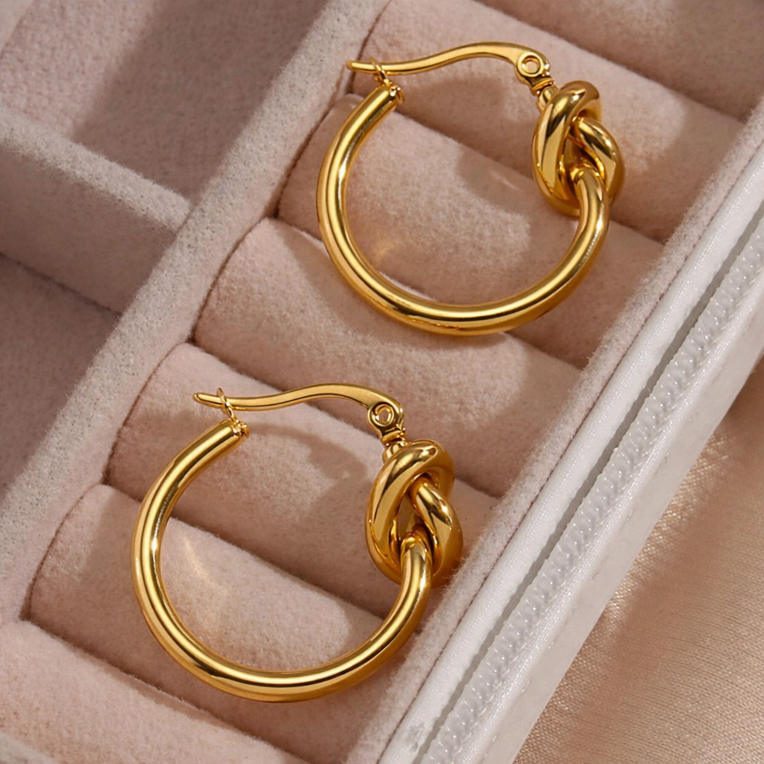 A pair of gold-plated hoop earrings for women featuring a central love-knot design, shown on a jewellery tray
